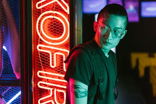 Stylish young man with eyeglasses in neon-lit futuristic setting, embodying cyberpunk fashion.