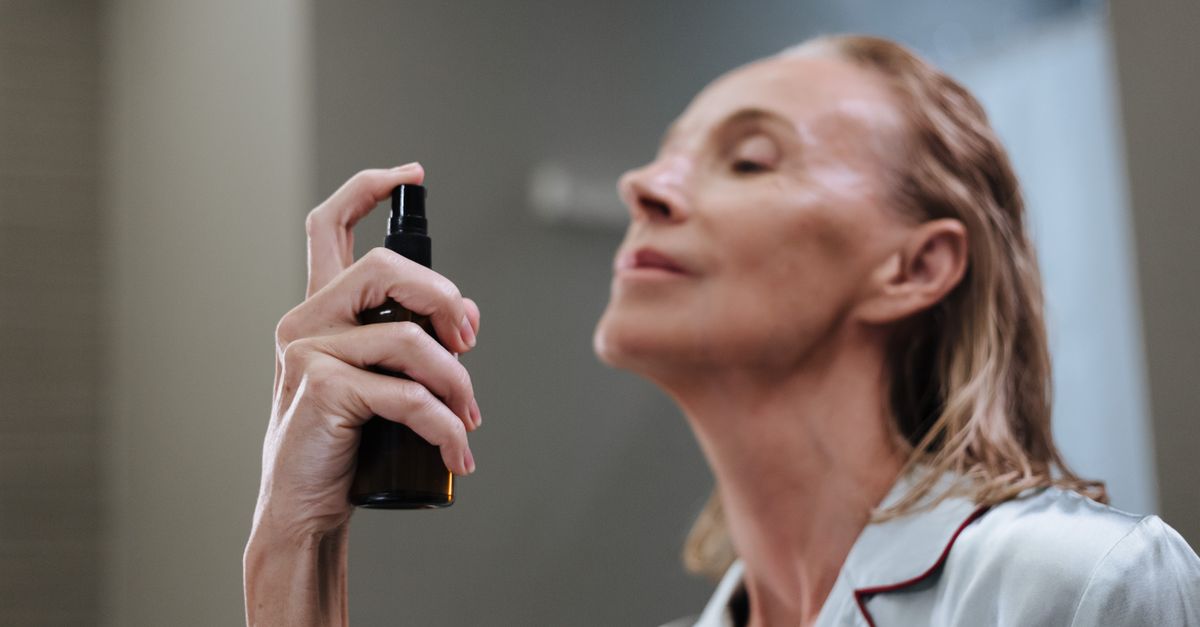 Senior woman demonstrating daily skincare routine, spraying face with a beauty product.