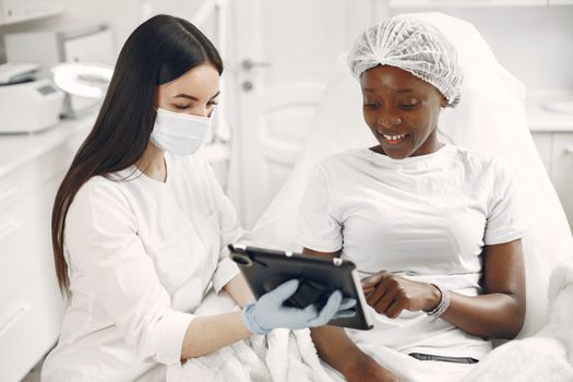 Smiling patient and dermatologist using tablet during skincare consultation.