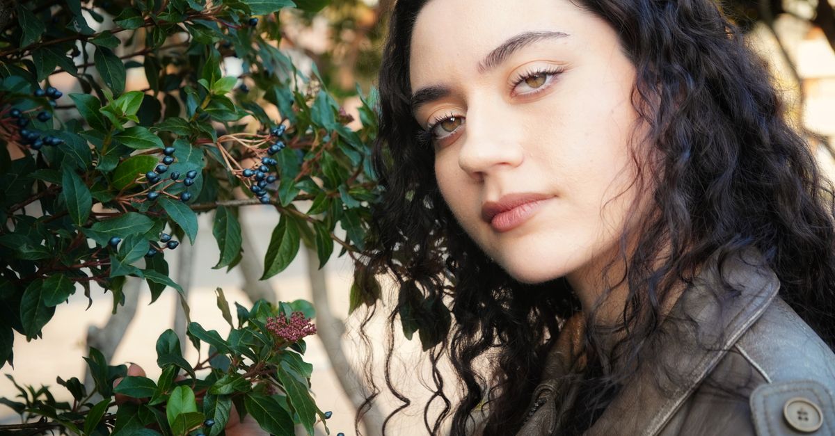 Portrait of a young woman with curly hair beside lush green foliage and berries.