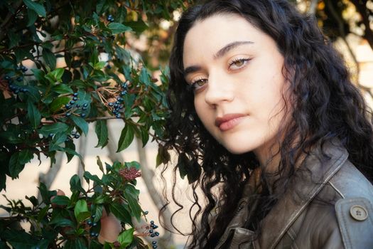 Portrait of a young woman with curly hair beside lush green foliage and berries.